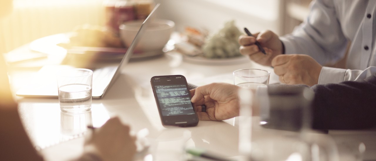 A table and people hands one holding a phone.